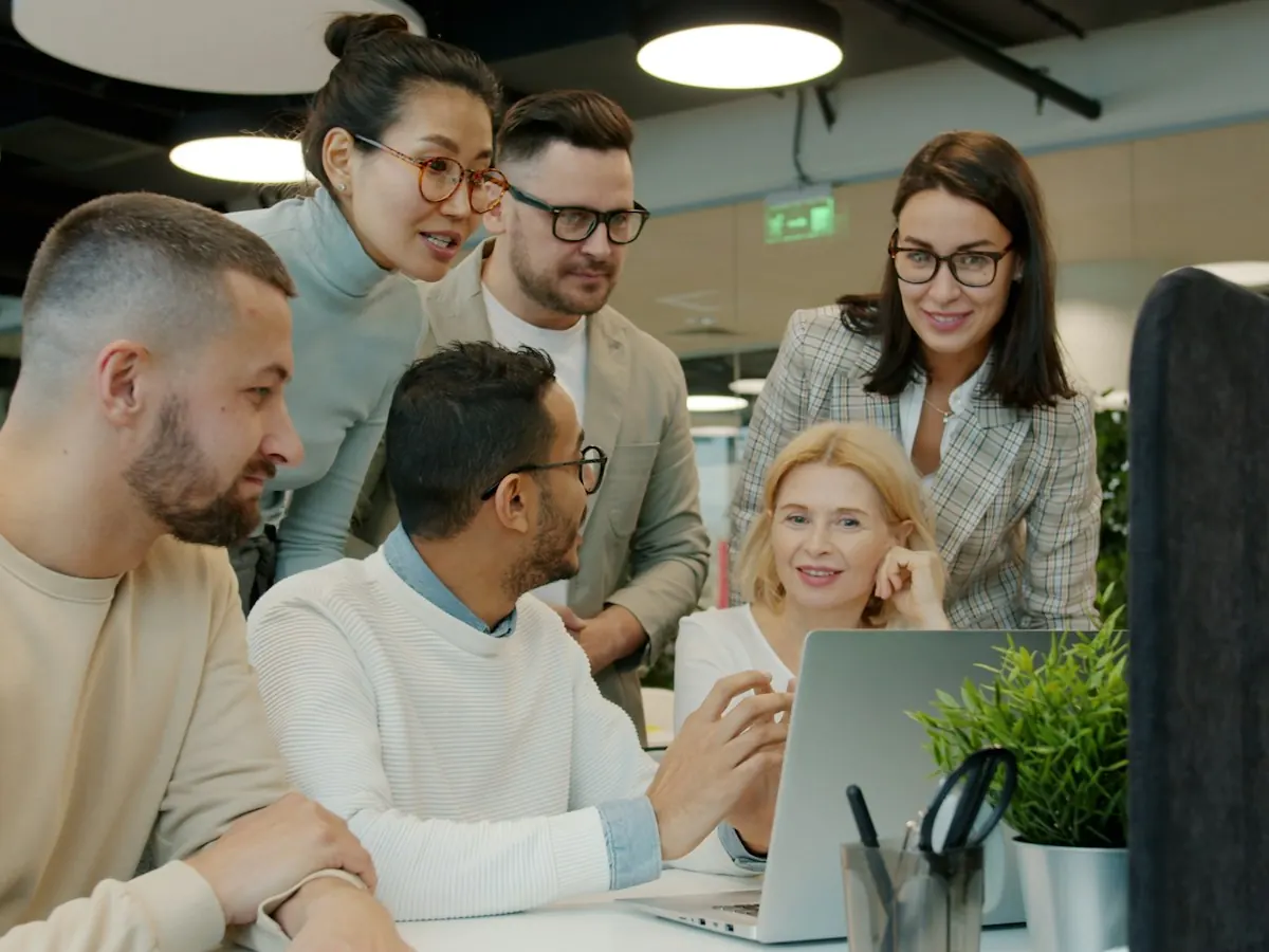 A mixed team gathered around a laptop in a bright office