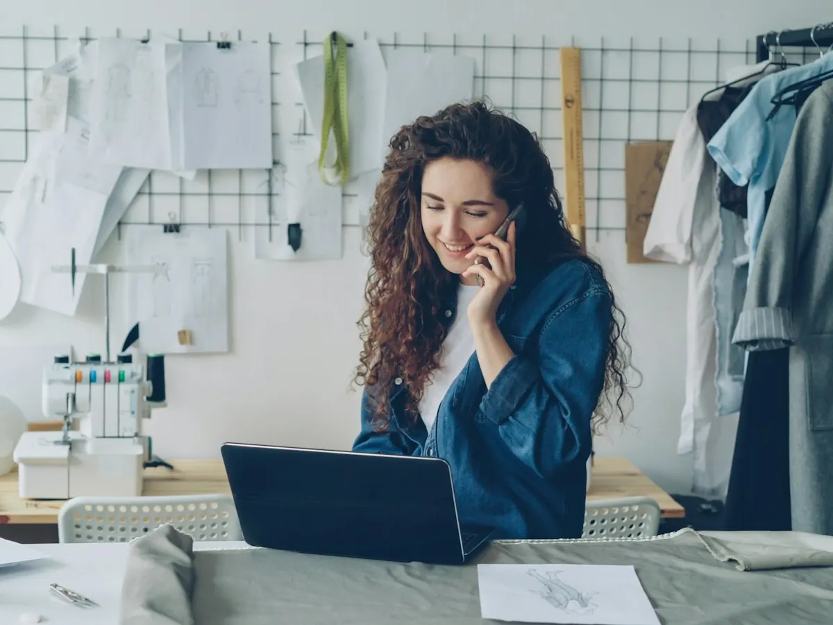 A business owner on the phone at her laptop in a small studio workroom