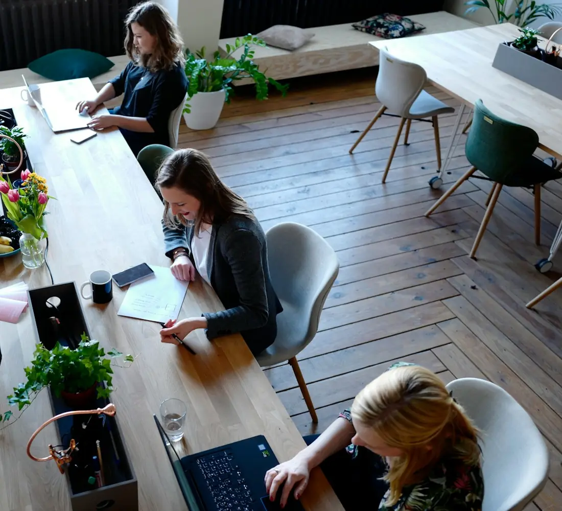 A small team working together at a long shared table in a bright workspace